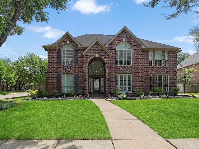 view of front of house featuring brick siding, a front yard, and roof with shingles