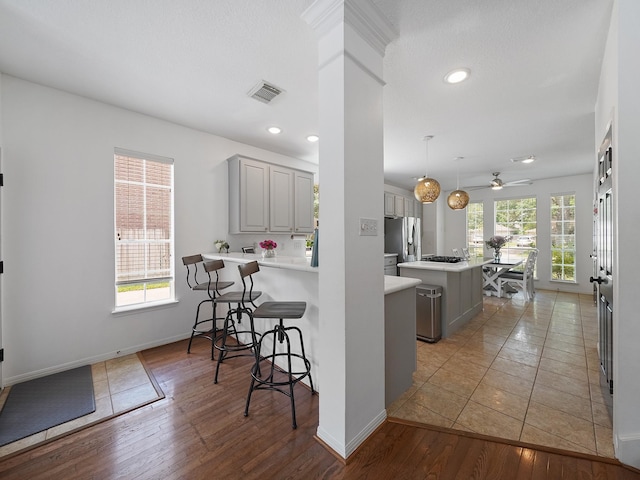 kitchen with visible vents, a kitchen island, a kitchen bar, gray cabinets, and stainless steel fridge with ice dispenser