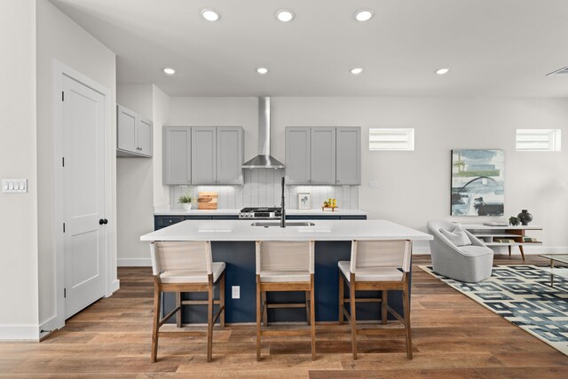 kitchen featuring wood finished floors, wall chimney range hood, gray cabinets, tasteful backsplash, and a sink