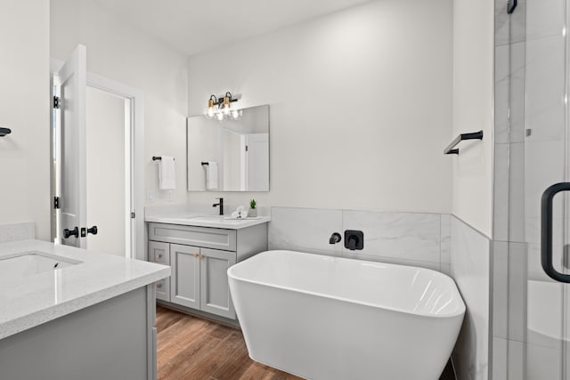 full bath with a freestanding bath, a sink, a shower with shower door, two vanities, and wood finished floors