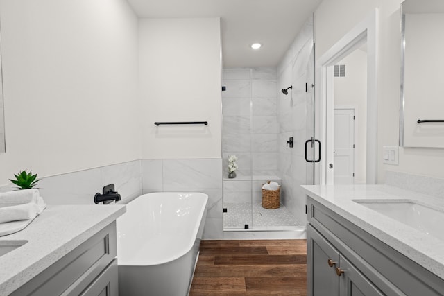 full bathroom featuring a freestanding tub, tile walls, a shower stall, two vanities, and recessed lighting