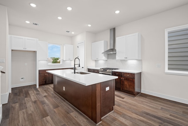 kitchen featuring wall chimney range hood, a sink, stainless steel range with gas cooktop, white cabinetry, and visible vents