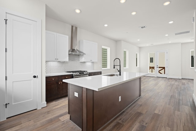 kitchen featuring wall chimney range hood, a kitchen island with sink, visible vents, light countertops, and a sink