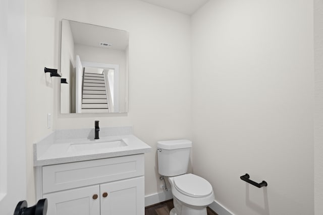 half bathroom featuring vanity, visible vents, wood finished floors, toilet, and baseboards