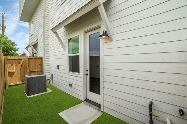doorway to property with fence, central AC unit, and a yard