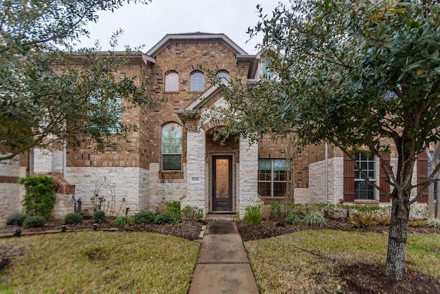 view of front facade featuring brick siding, a front lawn, and stone siding