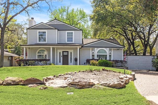 traditional-style home featuring covered porch, fence, a front lawn, a chimney, and a shingled roof