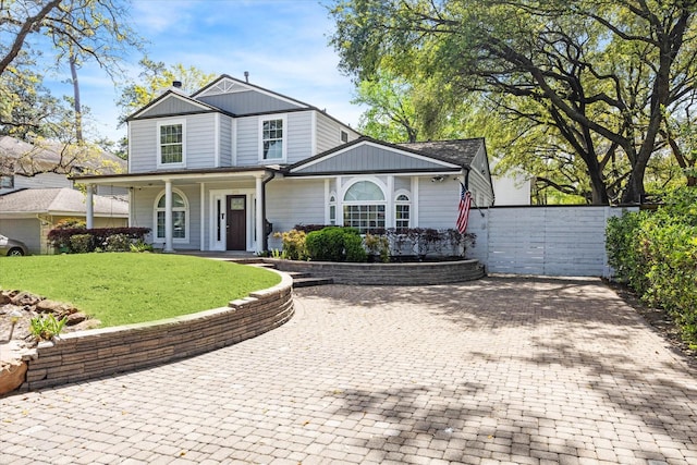 traditional-style home with covered porch, fence, a front lawn, and decorative driveway