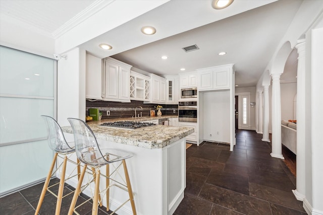 kitchen featuring a peninsula, backsplash, visible vents, ornate columns, and appliances with stainless steel finishes
