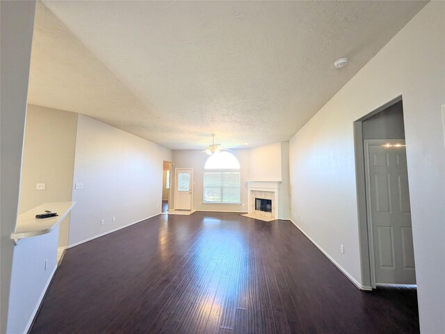 unfurnished living room with ceiling fan, a textured ceiling, hardwood / wood-style flooring, a tile fireplace, and baseboards