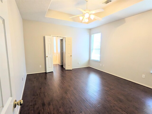 unfurnished room with visible vents, dark wood-style flooring, baseboards, ceiling fan, and a raised ceiling
