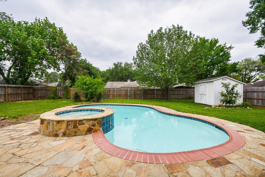 9730 Beversbrook Dr, Houston, TX 77031 - view of swimming pool with a shed, a fenced backyard, an outbuilding, a pool with connected hot tub, and a lawn