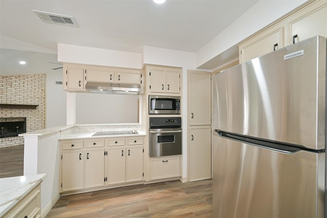 154 Camellia St, Sugar Land, TX 77478 - kitchen featuring stainless steel appliances, under cabinet range hood, light wood finished floors, a fireplace, and cream cabinetry
