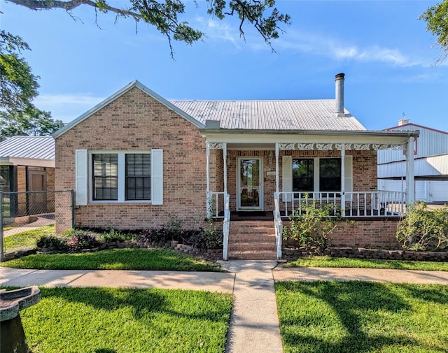 bungalow with fence, a front lawn, a porch, brick siding, and metal roof