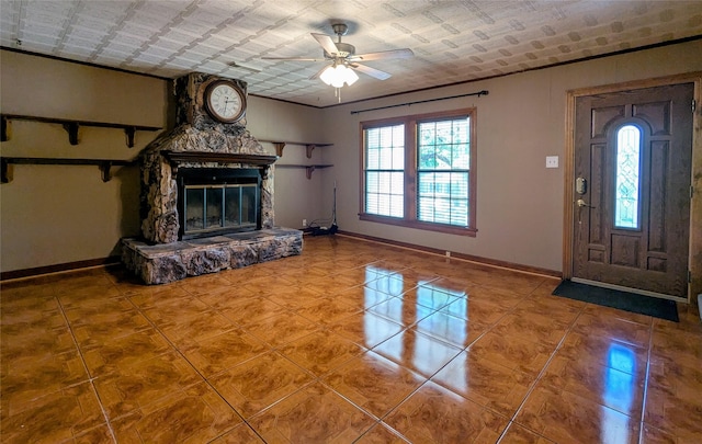 unfurnished living room with a stone fireplace, baseboards, a ceiling fan, and tile patterned floors