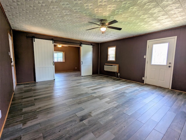 empty room with a barn door, a ceiling fan, wood finished floors, and a wall unit AC