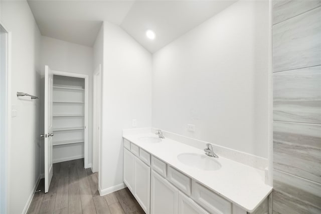 bathroom with wood finished floors, double vanity, a sink, and baseboards