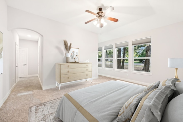 bedroom with arched walkways, light colored carpet, baseboards, and ceiling fan