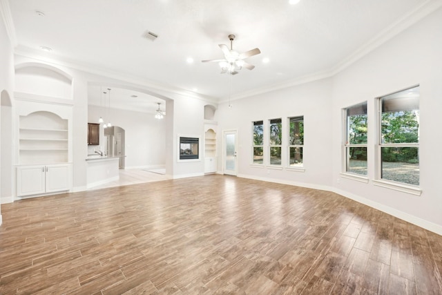 unfurnished living room featuring visible vents, ceiling fan with notable chandelier, built in features, and crown molding