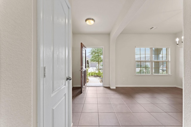 interior space featuring light tile patterned floors, baseboards, a textured wall, and visible vents