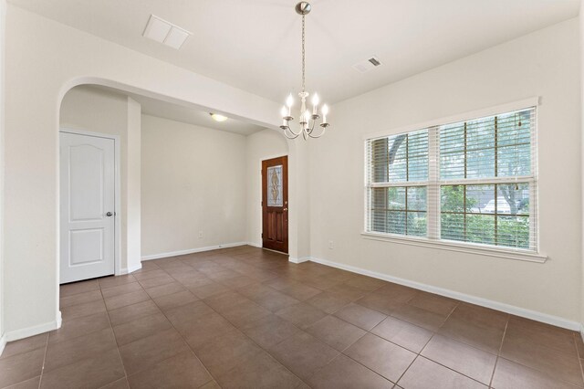 spare room featuring visible vents, arched walkways, dark tile patterned floors, and an inviting chandelier