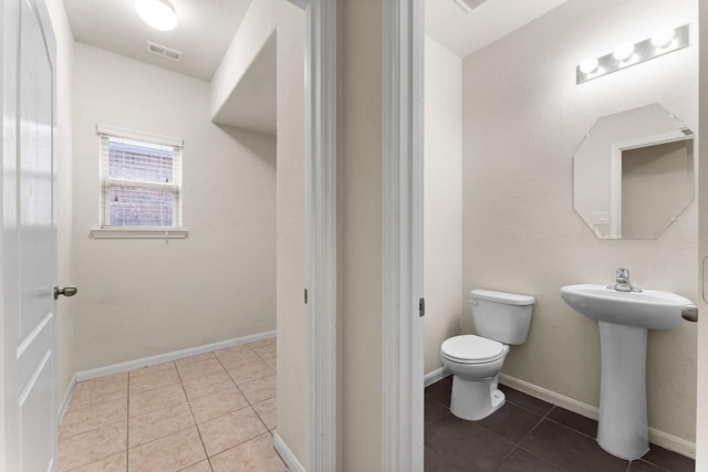 half bath with toilet, visible vents, a sink, and tile patterned flooring