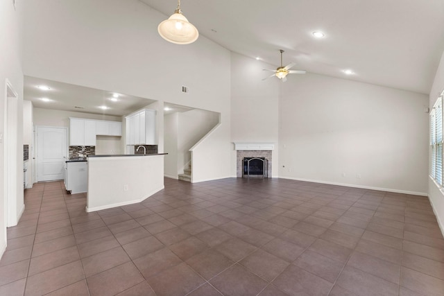 unfurnished living room with a fireplace, high vaulted ceiling, recessed lighting, dark tile patterned floors, and a ceiling fan