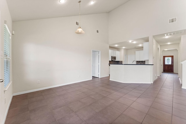kitchen with dark countertops, arched walkways, high vaulted ceiling, stainless steel microwave, and visible vents