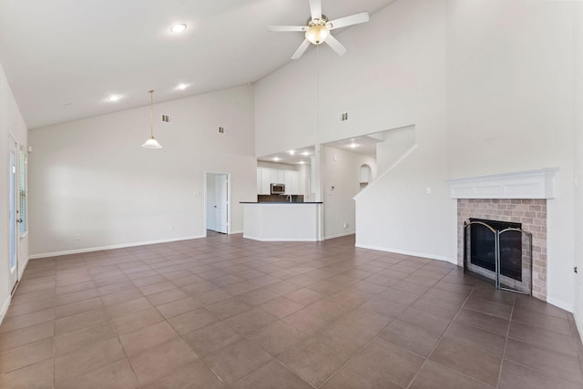 unfurnished living room with ceiling fan, tile patterned flooring, a brick fireplace, high vaulted ceiling, and baseboards