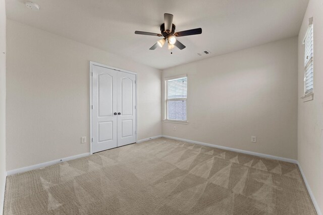 empty room with visible vents, baseboards, ceiling fan, and light carpet