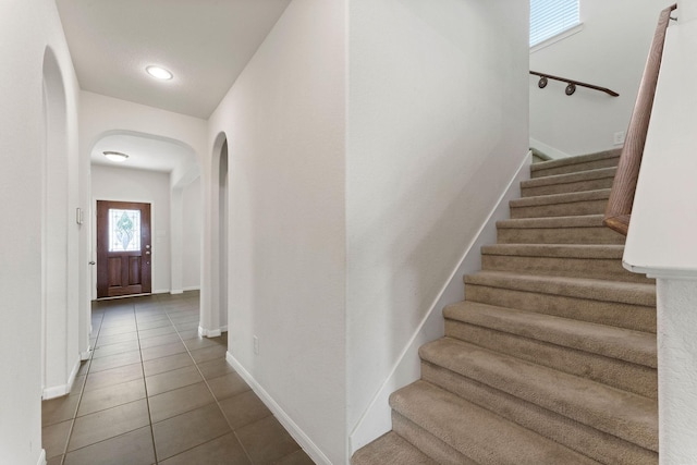stairs with arched walkways, baseboards, and tile patterned floors