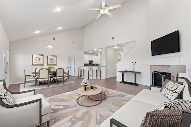 living room featuring ceiling fan, a brick fireplace, high vaulted ceiling, baseboards, and light tile patterned floors