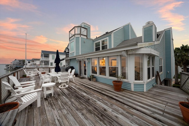 rear view of property featuring outdoor dining space, a deck, a shingled roof, and a chimney