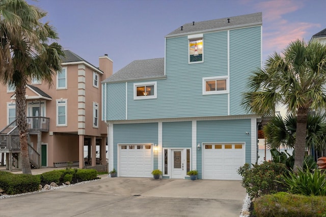 beach home featuring roof with shingles, driveway, and an attached garage