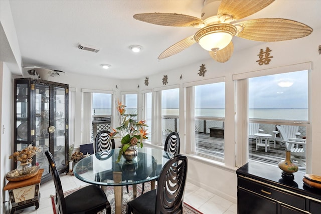 dining room featuring light tile patterned flooring, visible vents, ceiling fan, and a water view