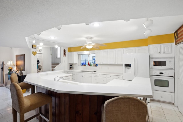 kitchen featuring white appliances, white cabinets, a sink, a ceiling fan, and a kitchen breakfast bar