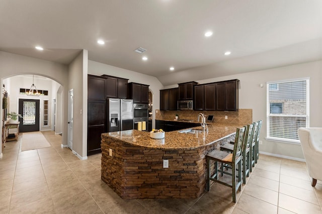 120 Brooke Addison Ct, Montgomery, TX 77316 - kitchen featuring dark brown cabinetry, arched walkways, stone counters, appliances with stainless steel finishes, and decorative backsplash