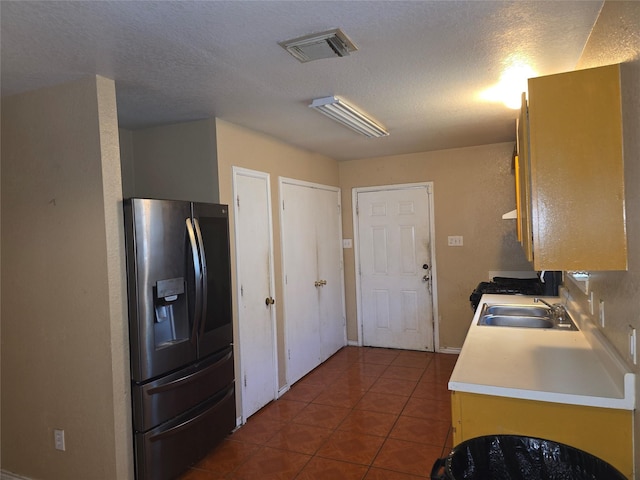 kitchen featuring visible vents, stainless steel refrigerator with ice dispenser, a sink, light countertops, and dark tile patterned flooring