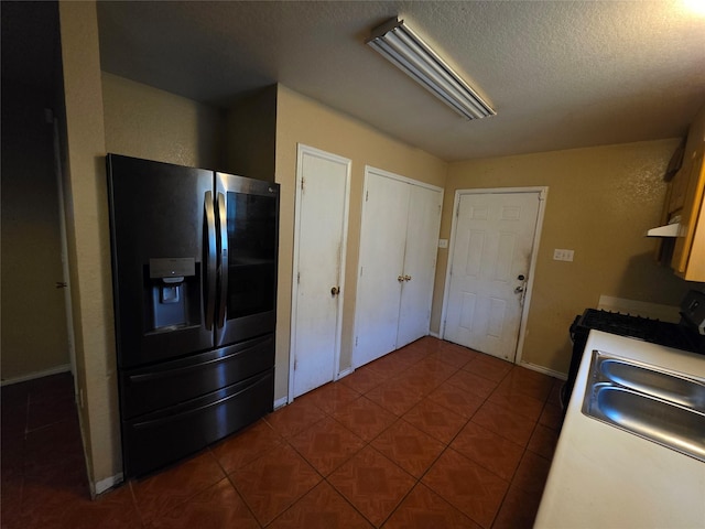 kitchen featuring fridge with ice dispenser, a textured ceiling, under cabinet range hood, dark tile patterned floors, and baseboards
