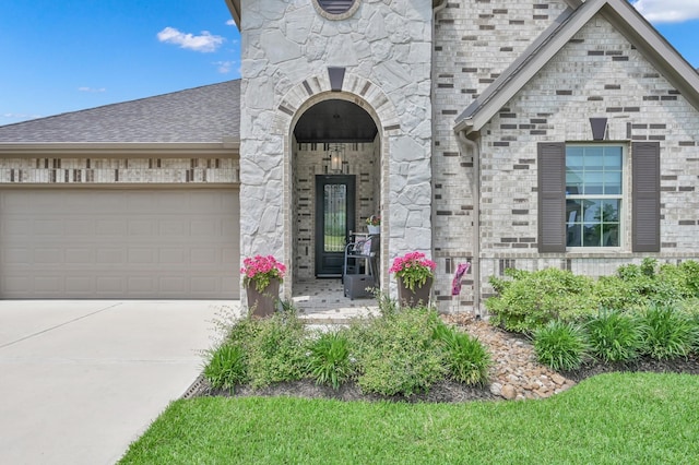 entrance to property with a garage, brick siding, roof with shingles, and concrete driveway