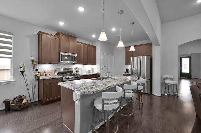 kitchen with arched walkways, a sink, a kitchen breakfast bar, stainless steel appliances, and dark wood-type flooring