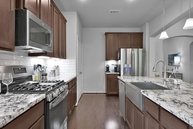 kitchen featuring visible vents, appliances with stainless steel finishes, light stone counters, a sink, and dark wood-style floors