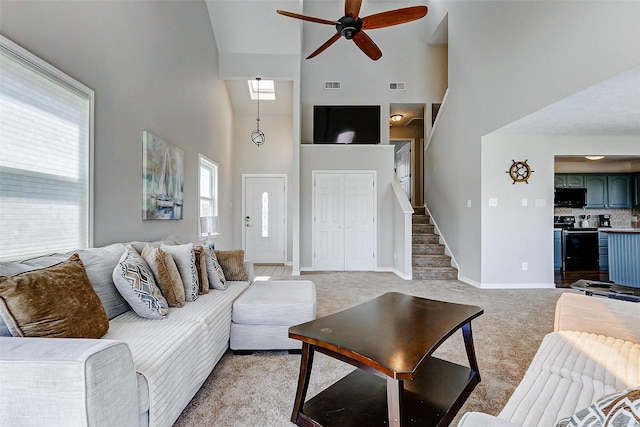 living area featuring a high ceiling, light colored carpet, ceiling fan, and visible vents