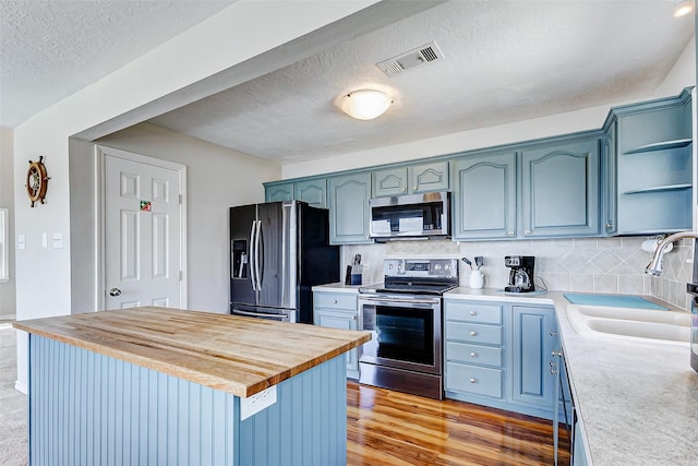 kitchen featuring butcher block counters, open shelves, visible vents, appliances with stainless steel finishes, and a sink