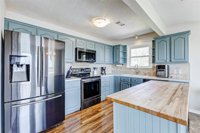 kitchen with visible vents, open shelves, a sink, a textured ceiling, and stainless steel appliances