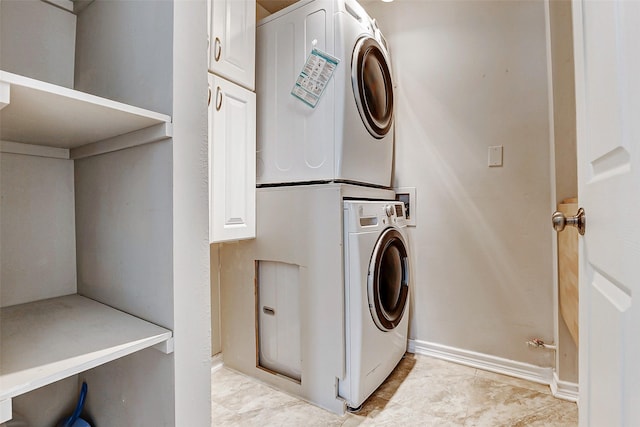 washroom with cabinet space, baseboards, and stacked washer / drying machine
