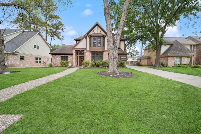 english style home with roof with shingles, a front yard, brick siding, and concrete driveway