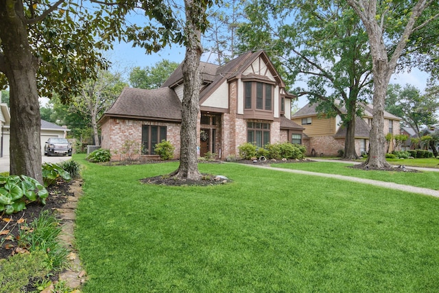 tudor house featuring a front yard, brick siding, a garage, and roof with shingles