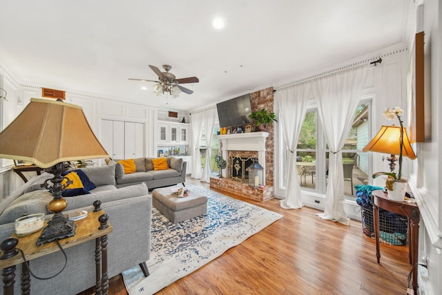 living room with a fireplace, a ceiling fan, ornamental molding, and wood finished floors