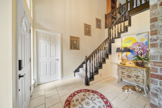 tiled foyer entrance with a towering ceiling, baseboards, and stairway